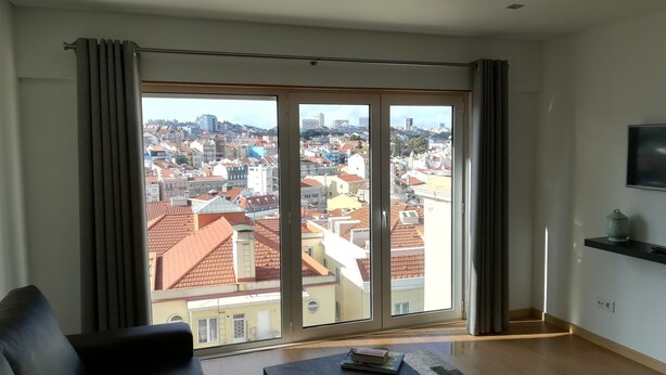 A modern living room with a large sliding glass door leading to a city view. - Lisbon Grand View (Lisboa)
