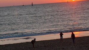 Una playa al atardecer con cielo despejado, mar tranquilo y algunos veleros.