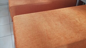 Habitación con dos camas cubiertas con ropa de cama naranja, un radiador blanco, una ventana con cortinas a rayas y un cabecero gris.