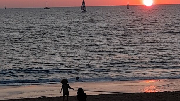 Un atardecer sobre un mar tranquilo con veleros.