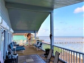 A covered outdoor area with a view of the ocean, featuring a wooden deck, several chairs, and a table. - Sophisticated, Beautiful Home! 3 BDRM/2 BATH. Private Fishing Pier. (Port Mansfield)