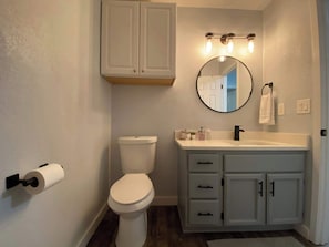 Un baño con inodoro, tocador con armarios y un espejo.