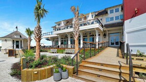 A beachfront property with a wooden deck, outdoor seating, and a building with multiple balconies. - Spacious, Pet-Friendly Home  Sea Pines Golf Views (Hilton Head Island)