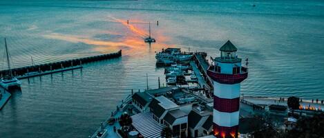 Una zona costera con un faro, barcos amarrados y un muelle que se adentra en el agua.