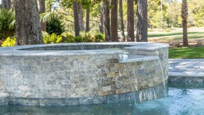 Une fontaine en pierre au design incurvé, entourée d’arbres et d’une zone herbeuse.