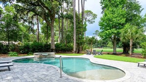 A swimming pool with a stone edge, surrounded by a paved deck, and trees in the background. - Spacious, Pet-Friendly Home  Sea Pines Golf Views (Hilton Head Island)