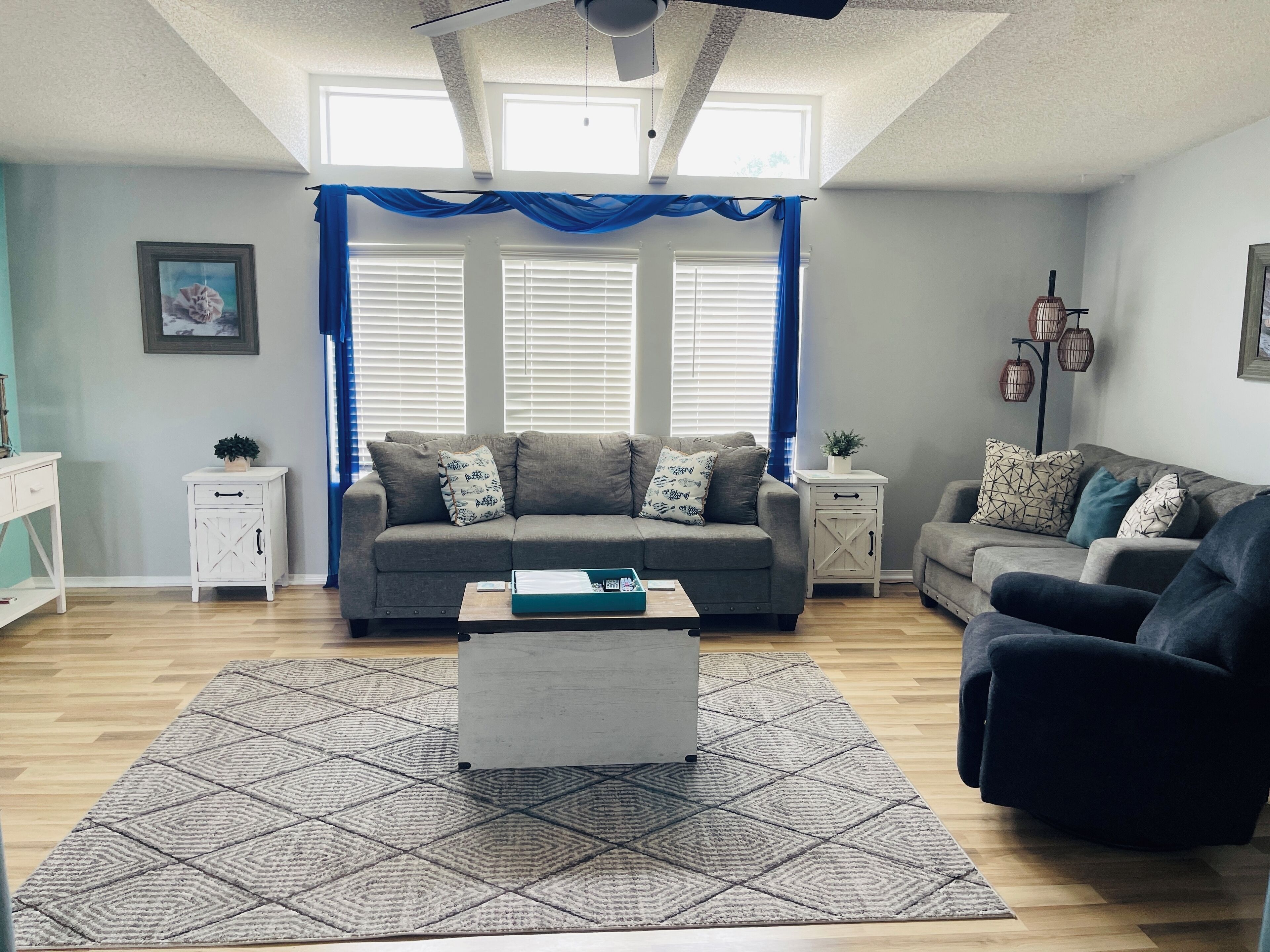 A living room with a grey sofa, a black armchair, a patterned rug, and a white coffee table.