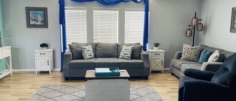 A living room with a grey sofa, a black armchair, a patterned rug, and a white coffee table.