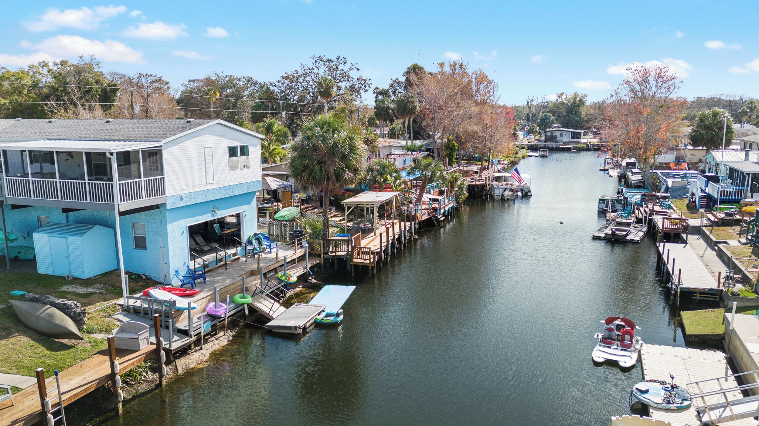 A marina with boats docked, a blue building with a balcony, and a river.