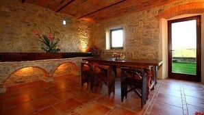 A rustic dining area with a stone wall, wooden table, and chairs. - Podere Lucignano Secondo - La Mangiatoia (Gaiole in Chianti)