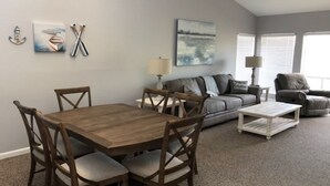 A living room with a wooden dining table, grey sofa, and a grey armchair. There are wall art pieces and a lamp. - CAROL'S GETAWAY near Sandy Beach (Heber Springs)