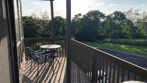 A wooden deck with a table and chairs, overlooking a green landscape and a road. - CAROL'S GETAWAY near Sandy Beach (Heber Springs)