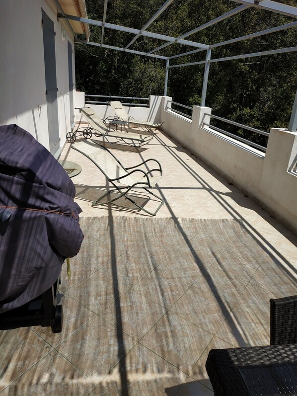 Una terraza en la azotea con un área de estar cubierta, una bicicleta y vistas a árboles.