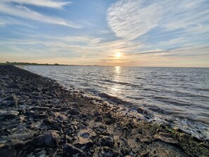 A rocky shoreline with a calm sea and a sunset in the background. - 5 persons - Beautiful and modern old town apartment in the heart of the city (Otterndorf)