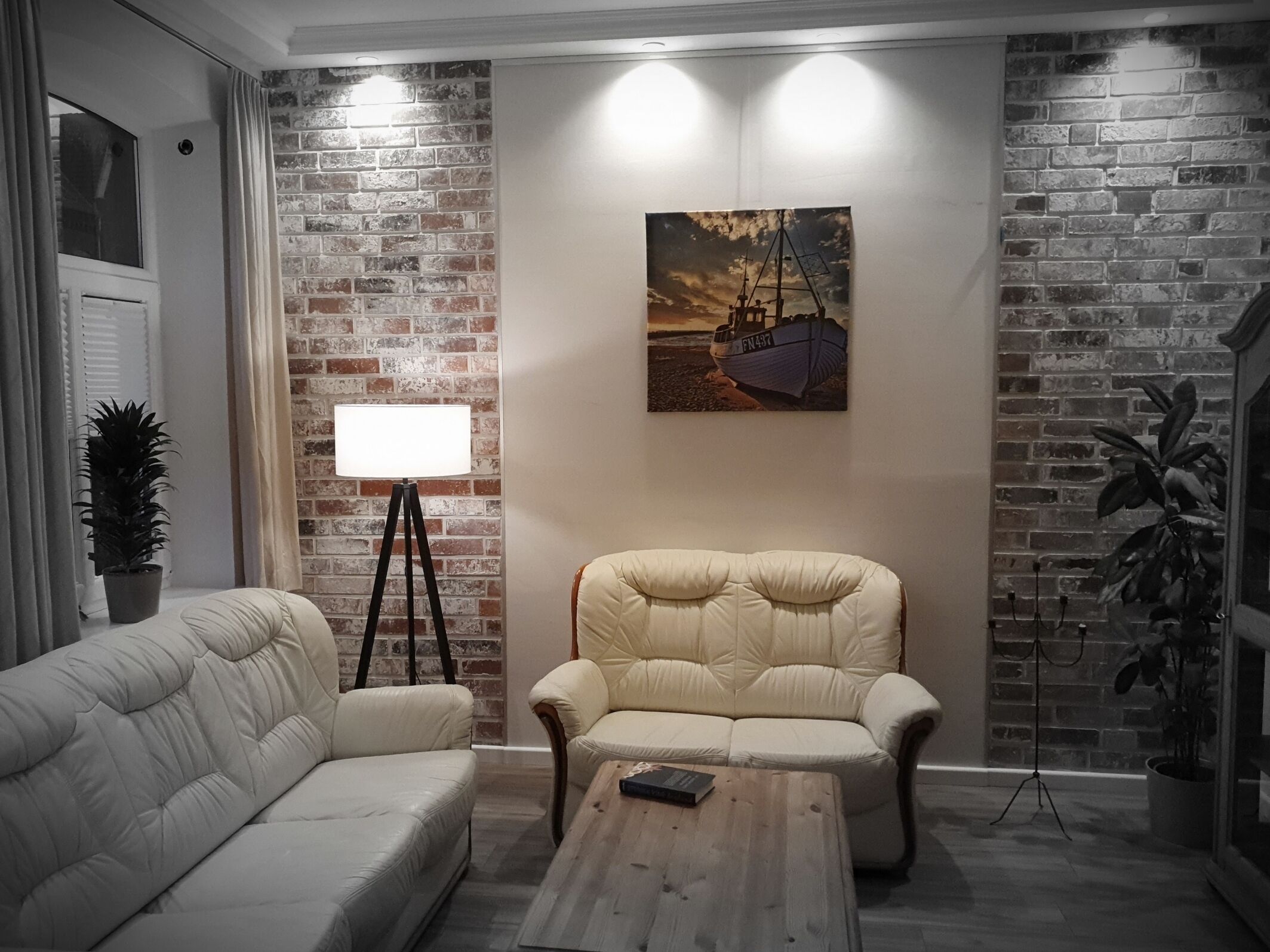 Ein Wohnzimmer mit Backsteinwand, einer Couch, einem Sessel, einem Couchtisch und einem Bild eines Bootes an der Wand.