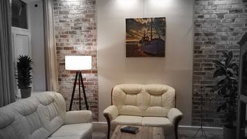 Ein Wohnzimmer mit Backsteinwand, einer Couch, einem Sessel, einem Couchtisch und einem Bild eines Bootes an der Wand.