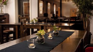 Un espace repas avec des tables et des chaises en bois, ainsi qu’un chemin de table noir. De petits vases en verre contenant des fleurs et des bougies sont disposés sur les tables.