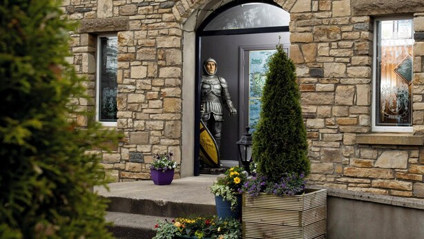 Un bâtiment en pierre, orné d’une statue de chevalier à l’entrée, un petit jardin avec des plantes en pot et une vue dégagée sur les environs.