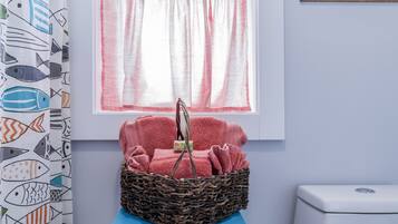 A bathroom with a blue sink, a white toilet, a wicker basket with pink towels, and a window with pink curtains.