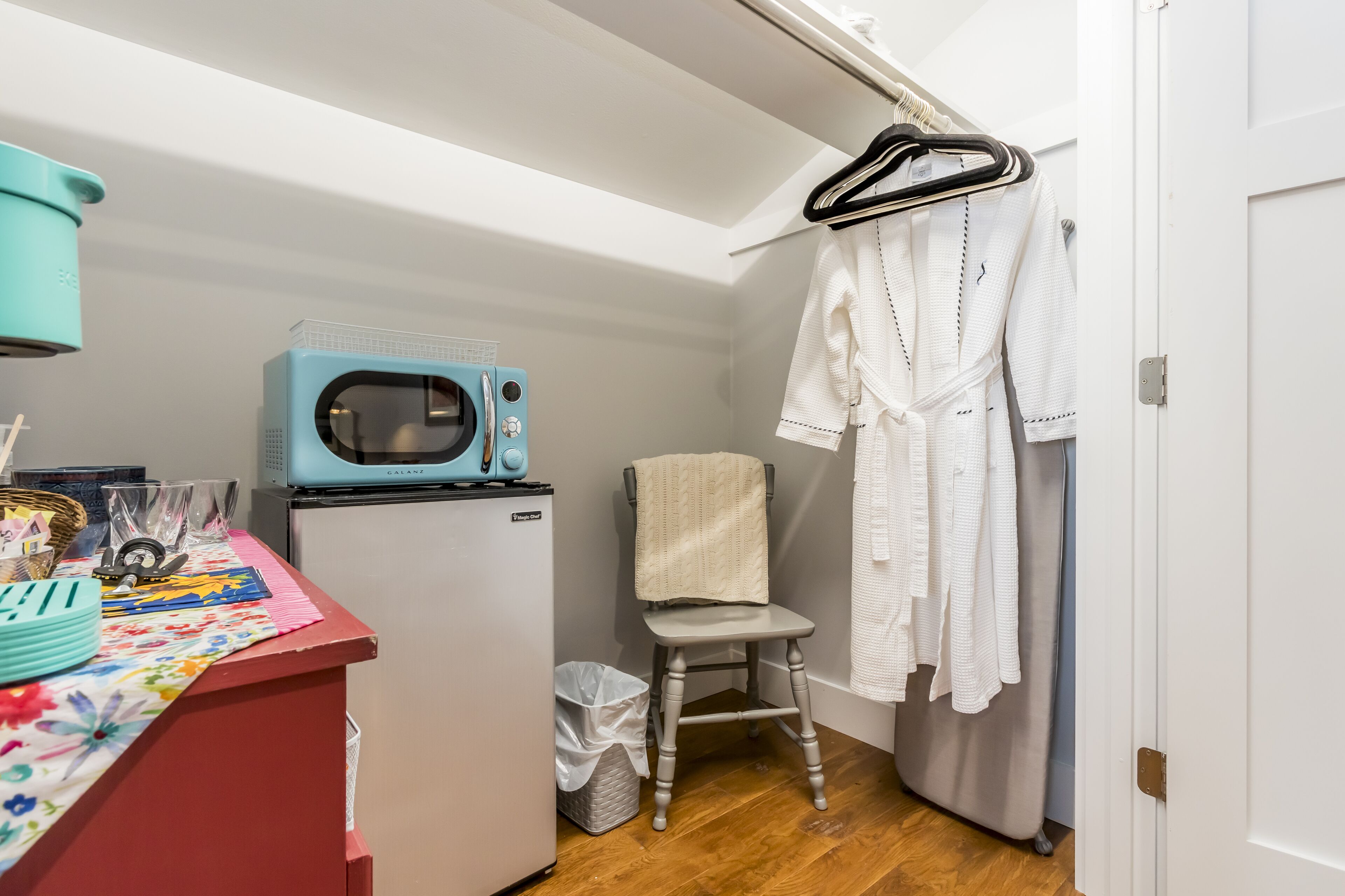 Ein gemütlicher Raum mit Mikrowelle, kleinem Kühlschrank, Stuhl und einem Koffergestell mit Bademänteln.