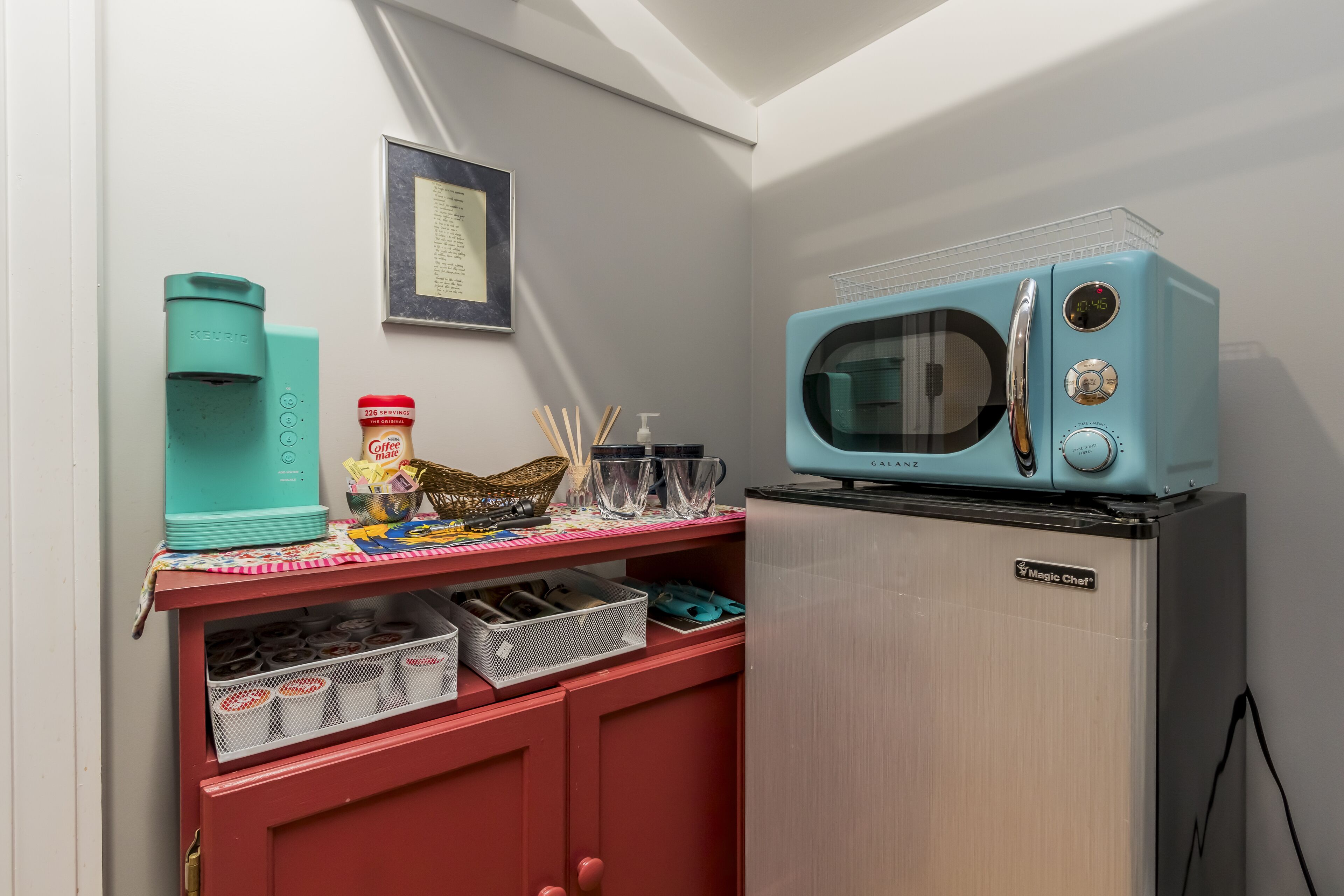 A kitchenette with a teal-colored microwave, a coffee maker, and a small refrigerator.