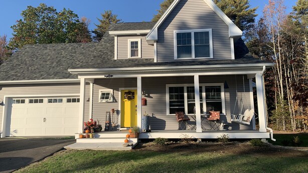 A two-story house with a covered porch, a garage, and a front yard with potted plants.