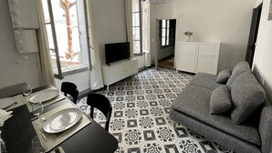 A modern living room with a grey sofa, a dining table set with plates and glasses, a TV on a stand, and patterned floor tiles. - L'appart Hyper Centre à 2 pas des Halles (Sète)