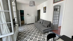 A modern living room with a grey sofa, patterned floor tiles, a hanging light fixture, and a white cabinet. - L'appart Hyper Centre à 2 pas des Halles (Sète)