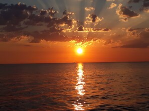 A sunset over a calm sea with a distant sailboat. - L'appart Hyper Centre à 2 pas des Halles (Sète)
