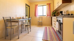 A kitchen with a dining table, chairs, a window with curtains, a stove, and a tiled floor.