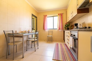 A kitchen with a dining table, chairs, a window with curtains, a stove, and a tiled floor.
