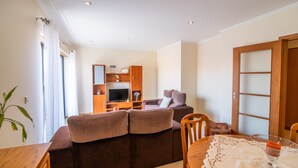 A living room with a brown sofa, a wooden TV stand, and a dining table with a lace tablecloth.