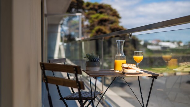 A balcony with a table set for breakfast, including bread, juice, and a small plant.