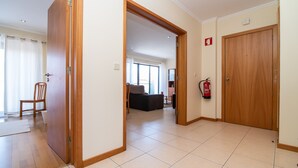 A hotel corridor with wooden doors, a fire extinguisher, and a view into a living area with a sofa and a window.