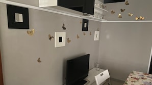A room with a flat-screen TV on a white stand, a small table with a floral tablecloth, and butterfly wall decals. - Plebiscito's House (Catania)