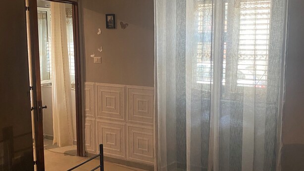 A bedroom with a bed, a mirror, a window with curtains, and a radiator. - Plebiscito's House (Catania)