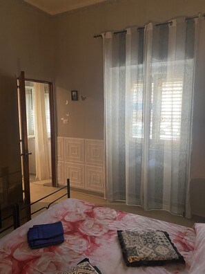 A bedroom with a bed, a mirror, a window with curtains, and a radiator. - Plebiscito's House (Catania)