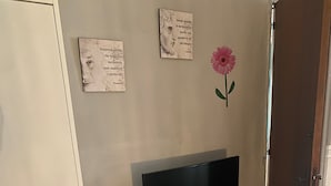 A room with a flat-screen TV on a black stand, a small table, a gray rug, and two framed quotes on the wall. - Plebiscito's House (Catania)