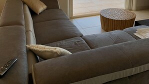 A modern living room with a large sofa, a small round table, and a view of the sea through a sliding glass door. - Villa Contemporaine D'exception à 5 min de Propriano (viggianello)