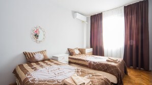 Un dormitorio con dos camas, una mesita de noche blanca, un espejo y una ventana con cortinas.
