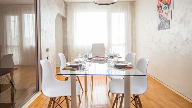 Un comedor moderno con una mesa de vidrio, sillas blancas y un ventanal con cortinas traslúcidas.