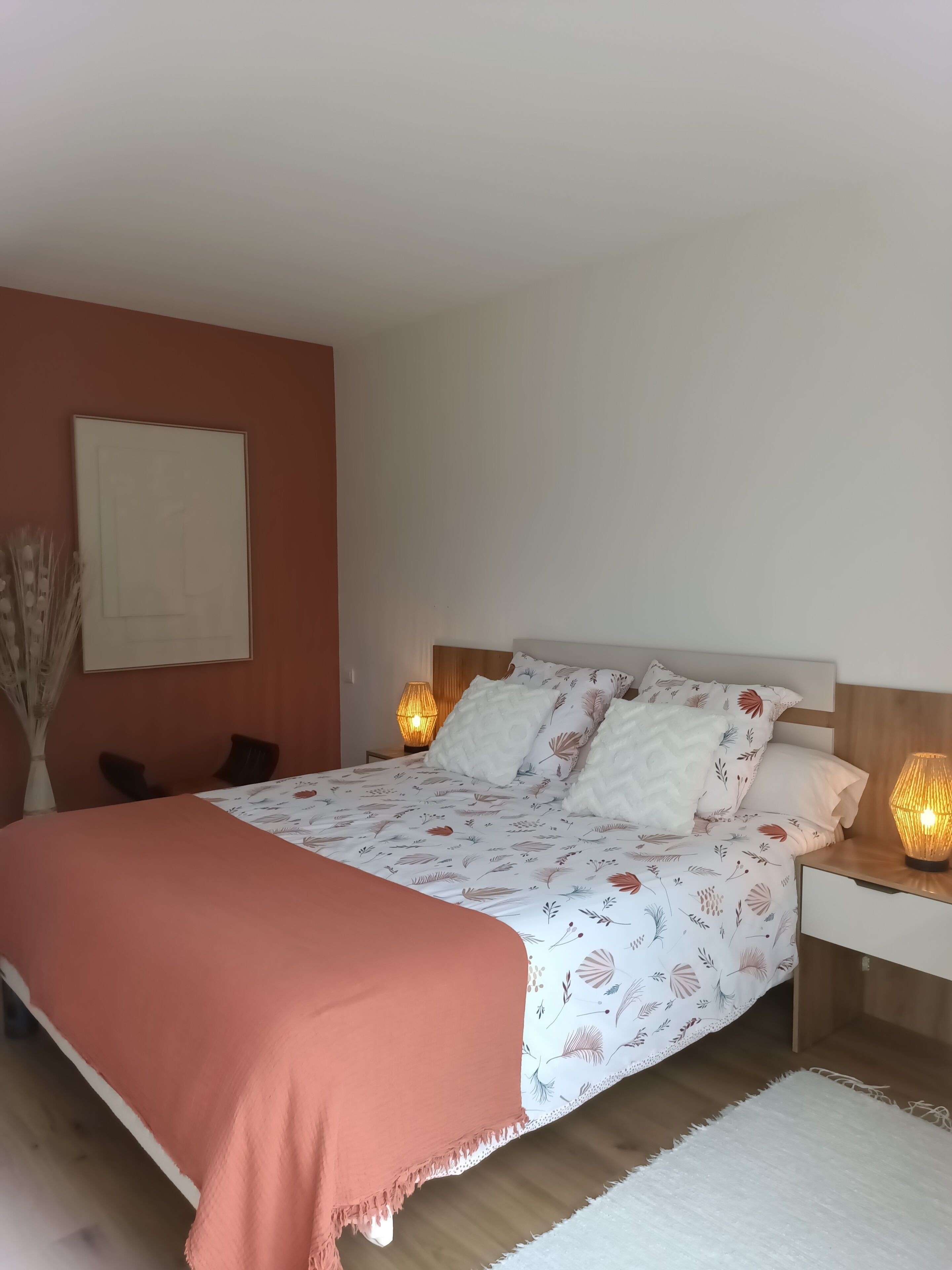 Une chambre à coucher comprenant un lit, des tables de chevet, une lampe fixée au mur et un vase décoratif.