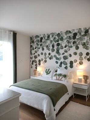 Et soveværelse med seng, to sengeborde, en lampe, et grønt tæppe og en væg med bladmotiver.