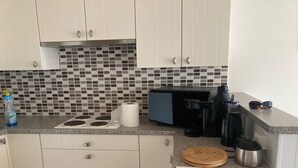 A compact kitchen with white cabinets, a tiled backsplash, a coffee maker, a kettle, and a cutting board. - Studio vue sur mer Avec Piscine Interieure (La Panne)