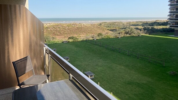 A balcony with a view of a grassy field and a distant beach. - Studio vue sur mer Avec Piscine Interieure (La Panne)