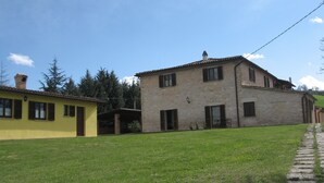 Une maison en pierre à deux étages, avec un toit en tuiles, un petit garage attenant et une allée pavée.