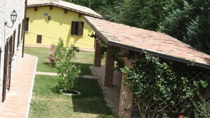 Un bâtiment jaune avec un toit en tuiles, un mur en briques et un petit jardin agrémenté de fleurs roses et d’une tonnelle.