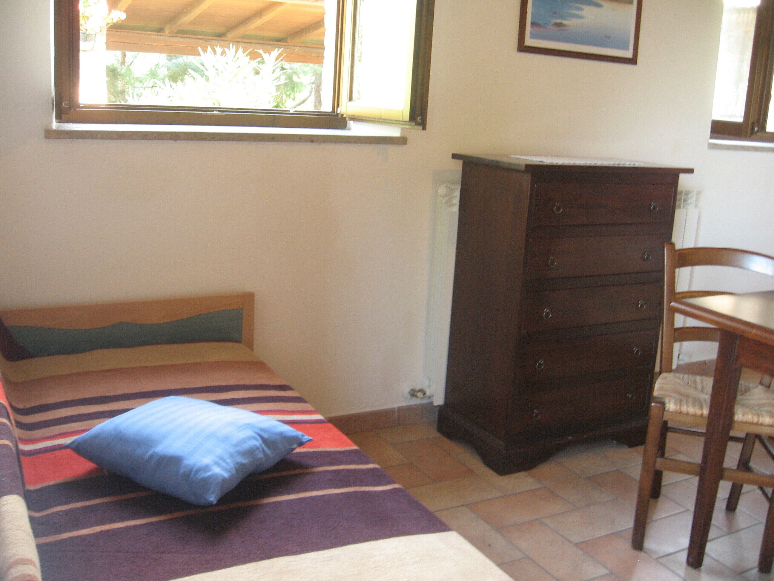 Ein kleines Zimmer mit einem Einzelbett, einem Holzschrank und einem Stuhl.
