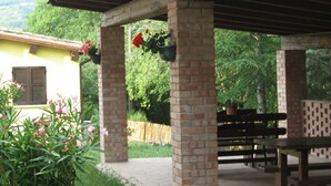 Un espace extérieur abrité, doté de piliers en briques, d’un banc en bois et de jardinières suspendues.