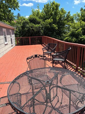 Une terrasse rouge avec une table ronde en métal et deux chaises en osier, entourée d’une rambarde rouge.